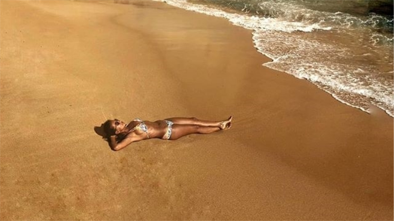 A apresentadora deitada à beira-mar numa praia deserta.
